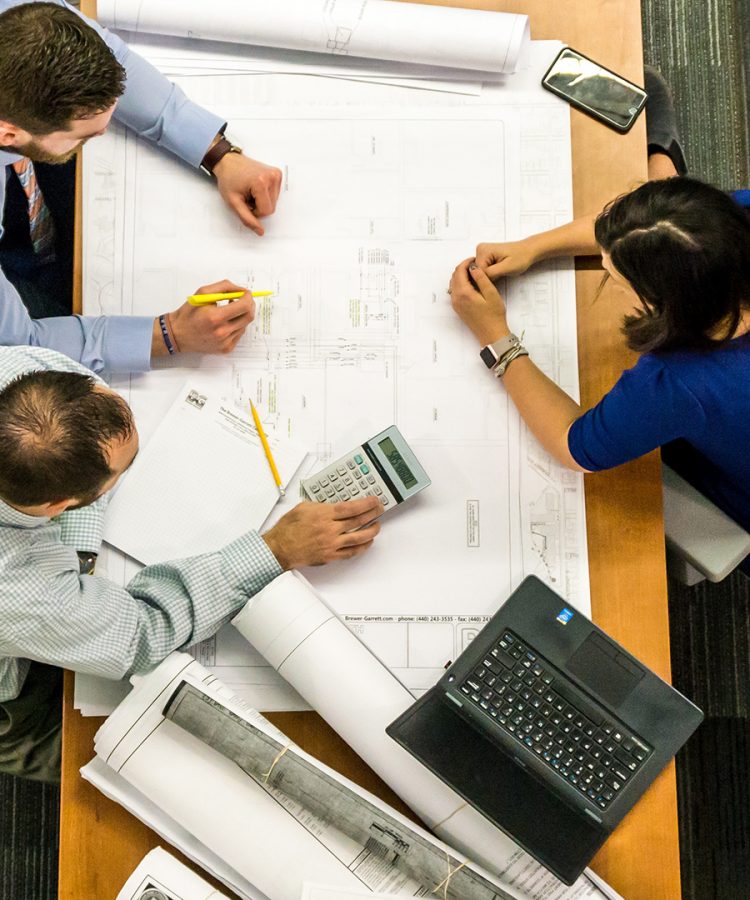 Three people working on a blueprint on a desk